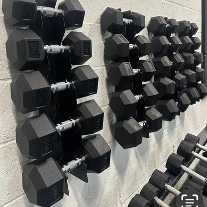 Hex dumbbell sets in varying weights neatly organized on two wall-mounted black metal racks against a gray wall.